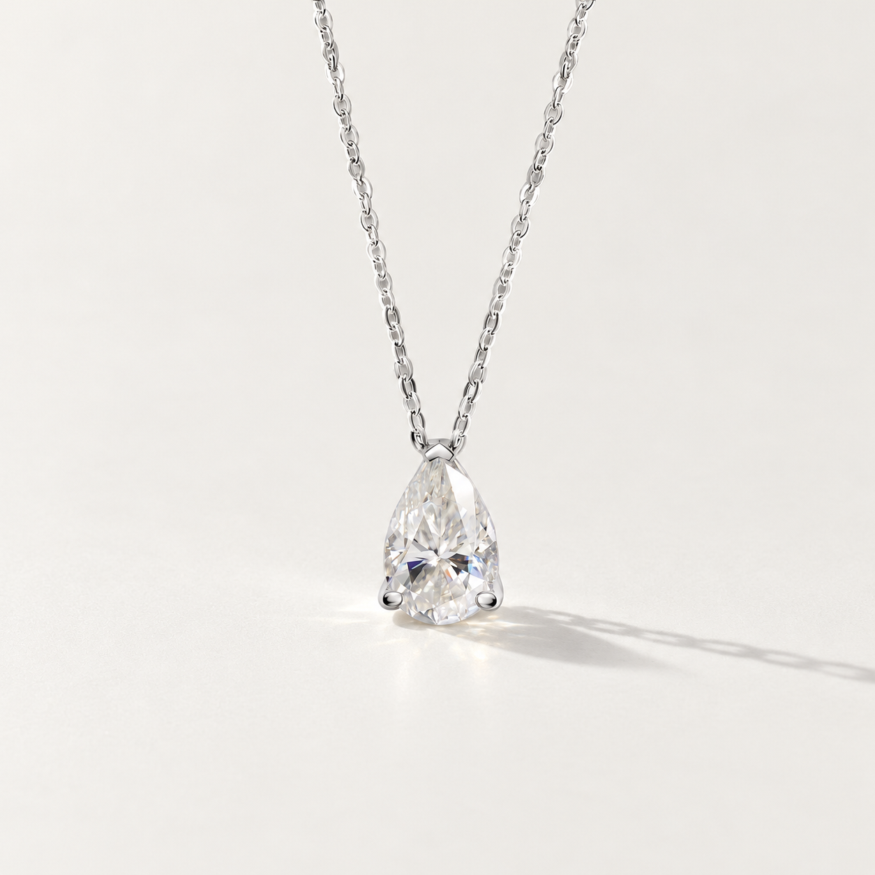 A pear-cut clear moissanite gemstone pendant necklace on a delicate silver chain, photographed against a clean off-white background with a soft shadow.