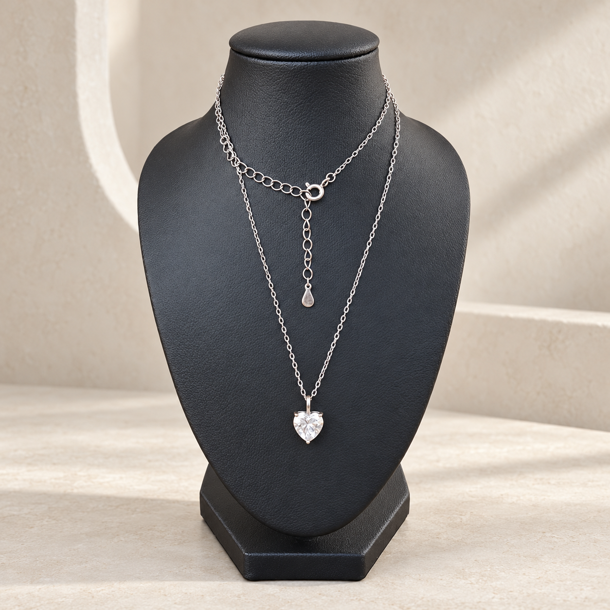 A layered silver necklace set displayed on a black jewelry bust. The set includes a longer chain with a small heart moissanite  charm pendant