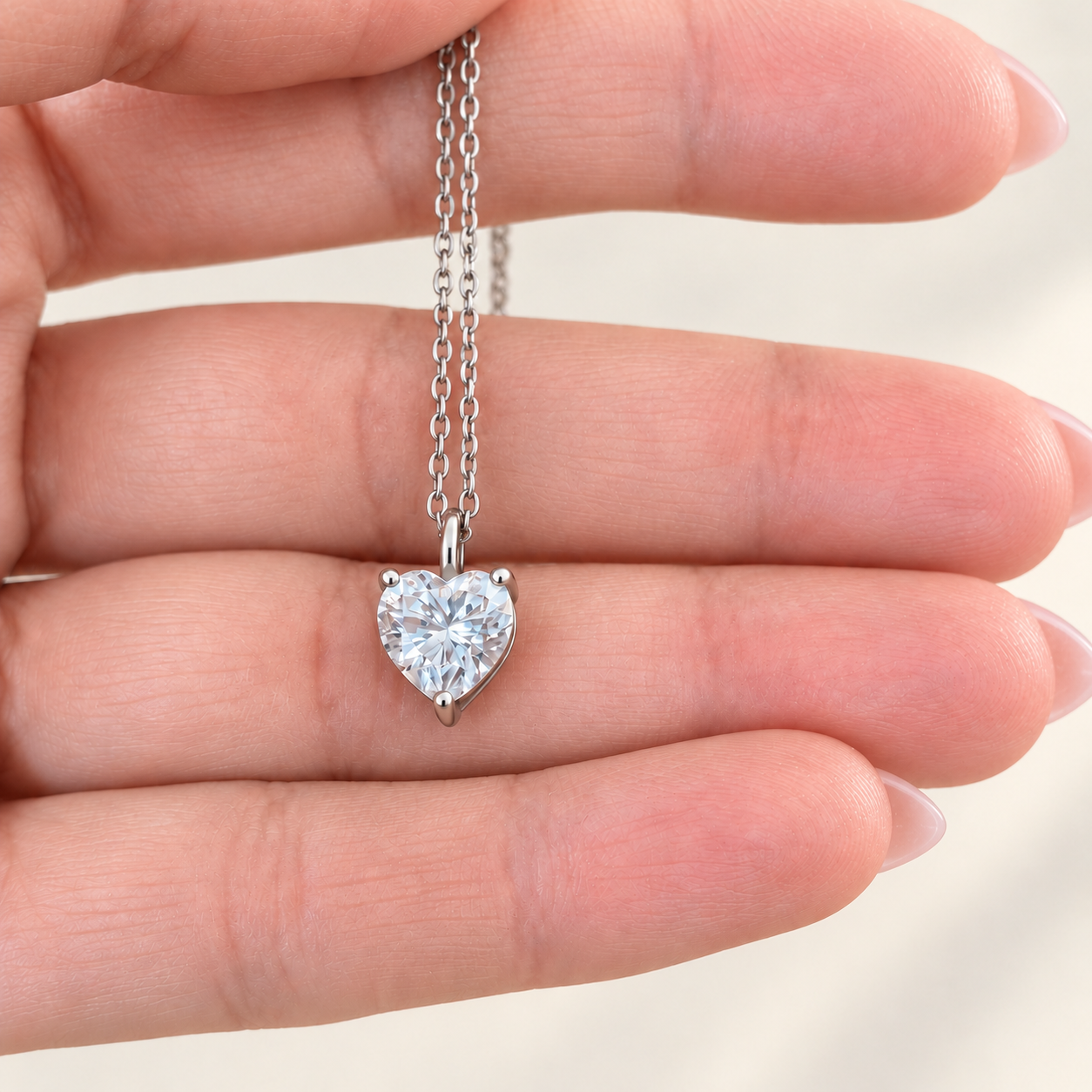 A heart-shaped clear moissanite gemstone pendant on a silver chain, held between fingers to show scale.