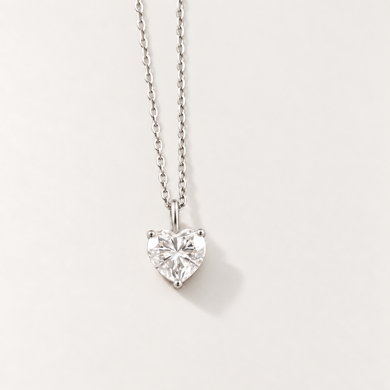 A silver heart-shaped pendant necklace with a clear heart-cut moissanite gemstone, suspended from a delicate silver chain against a light off-white background.
