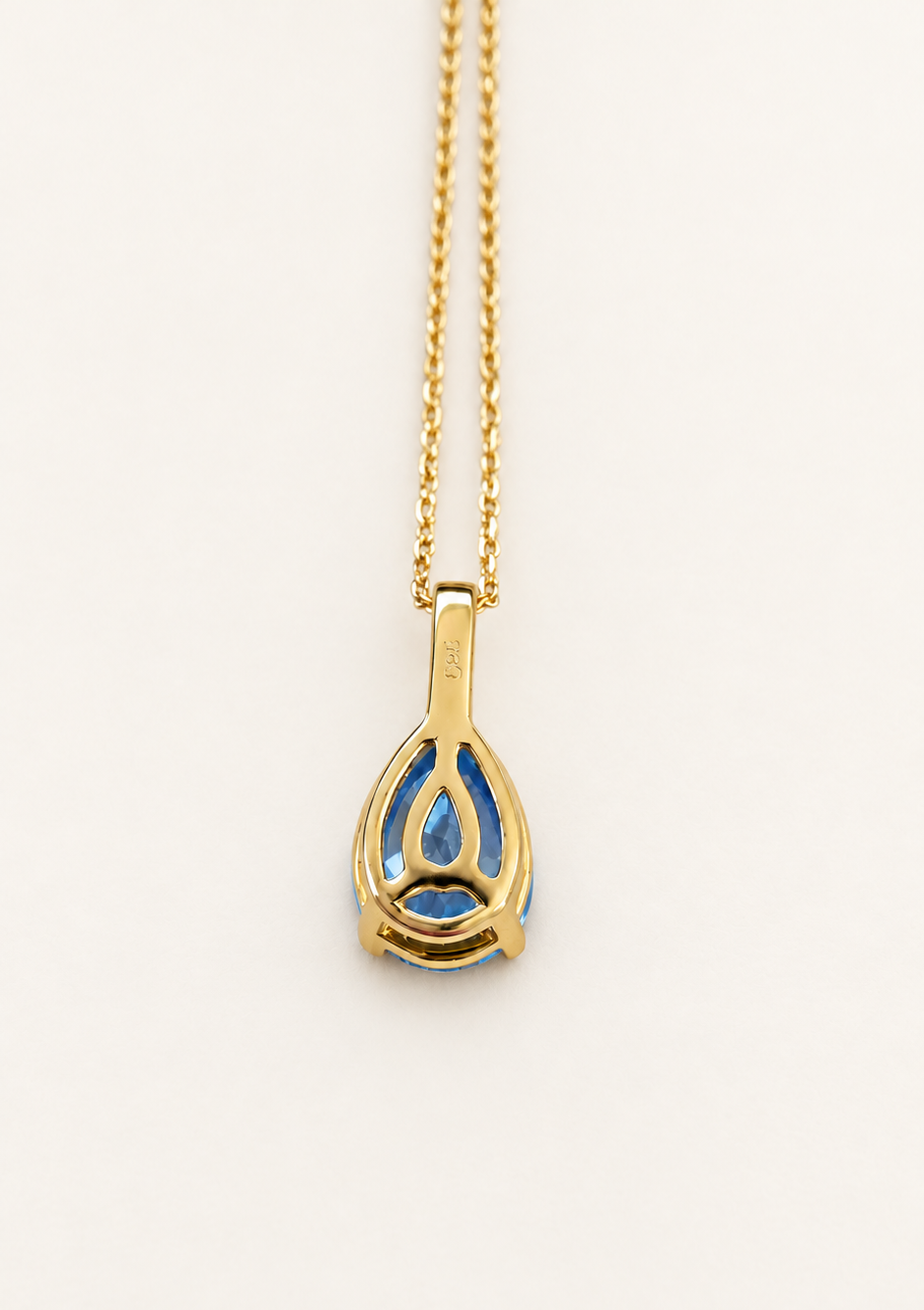 A gold pendant necklace with a teardrop-shaped design featuring blue topaz gemstone, shown against a plain white background.