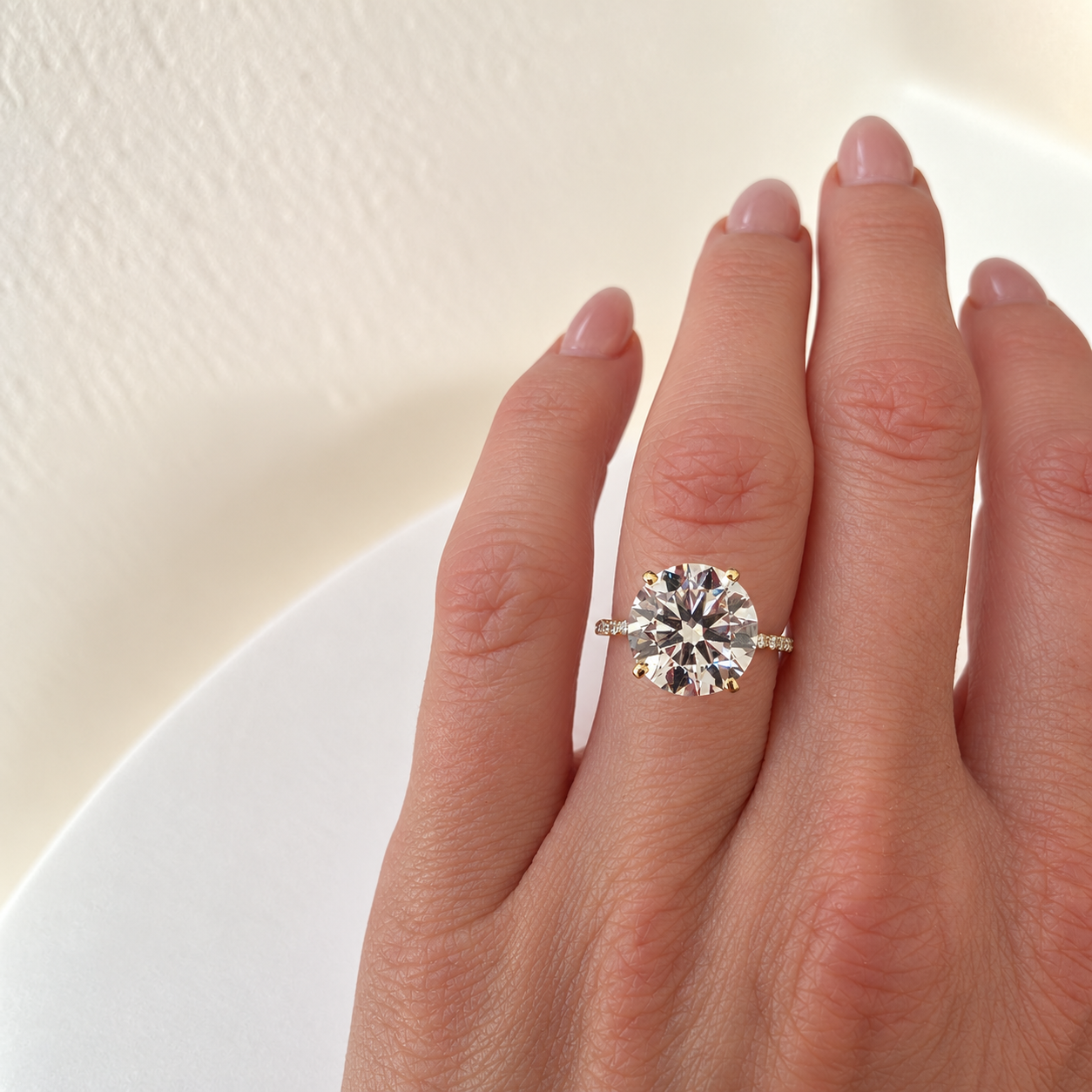 A yellow gold solitaire engagement ring with a large round brilliant-cut clear 4ct diamond center stone and a pavé-set diamond band, photographed on a clean white background with a soft shadow.