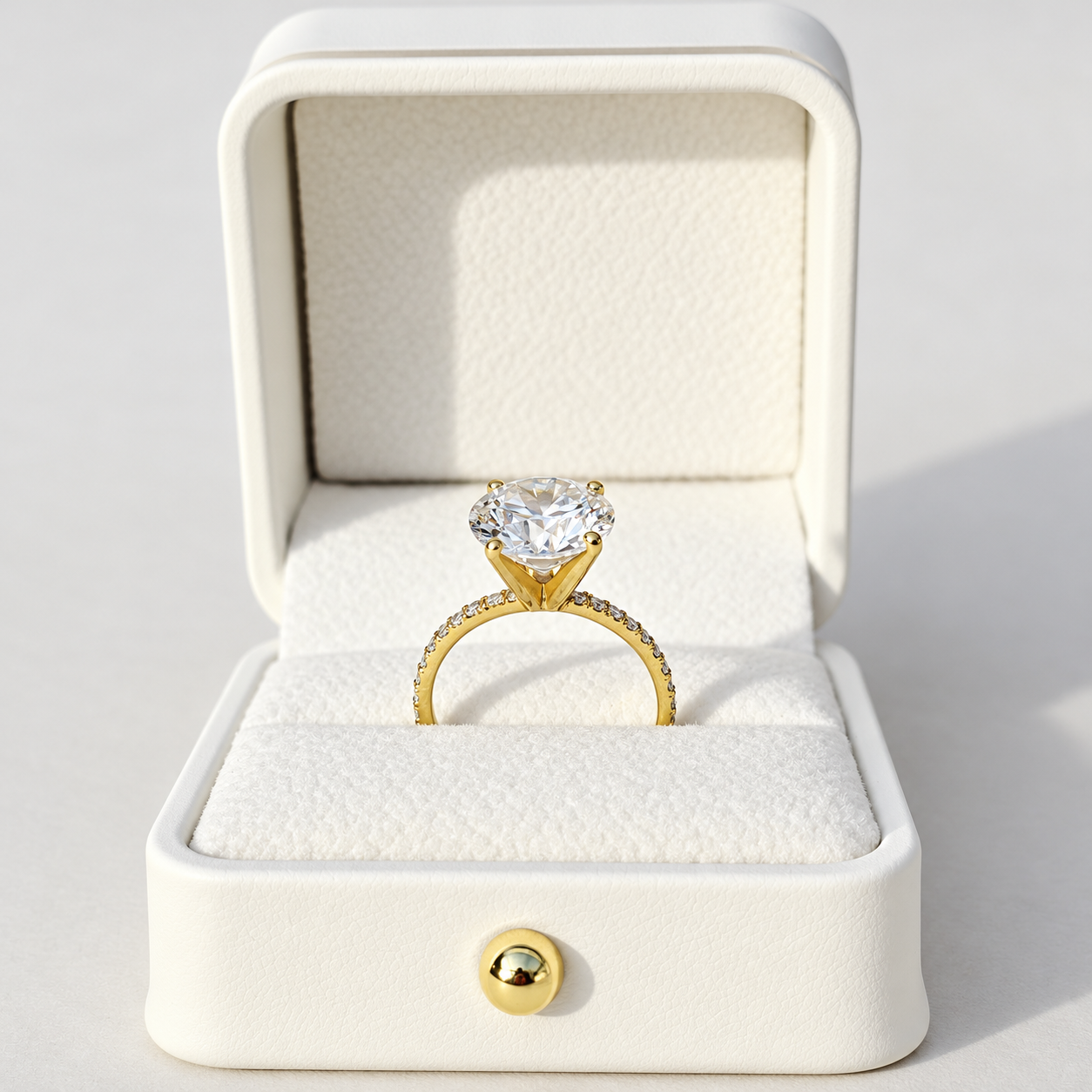 A yellow gold solitaire engagement ring with a large round brilliant-cut clear 4ct diamond center stone and a pavé-set diamond band, photographed on a clean white background with a soft shadow.