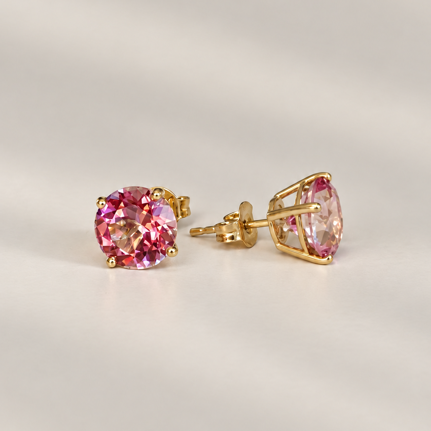 A pair of gold stud earrings featuring pink topaz gemstones, one shown from the front and the other from the side/back. The earrings are photographed on a clean, light beige background with soft shadows.