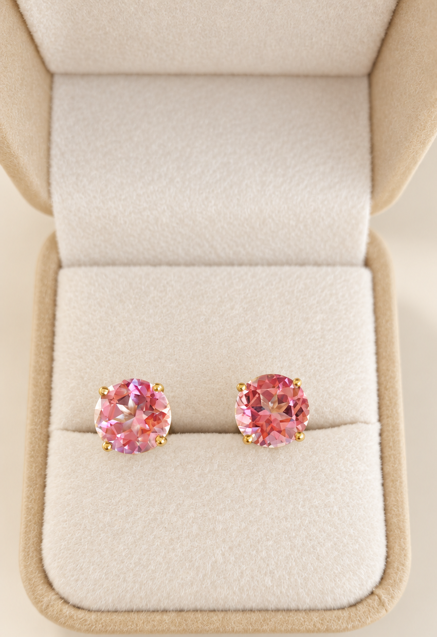 A pair of round pink topaz gemstone stud earrings in gold-toned settings, displayed in an open beige jewelry box on a soft cream velvet cushion.