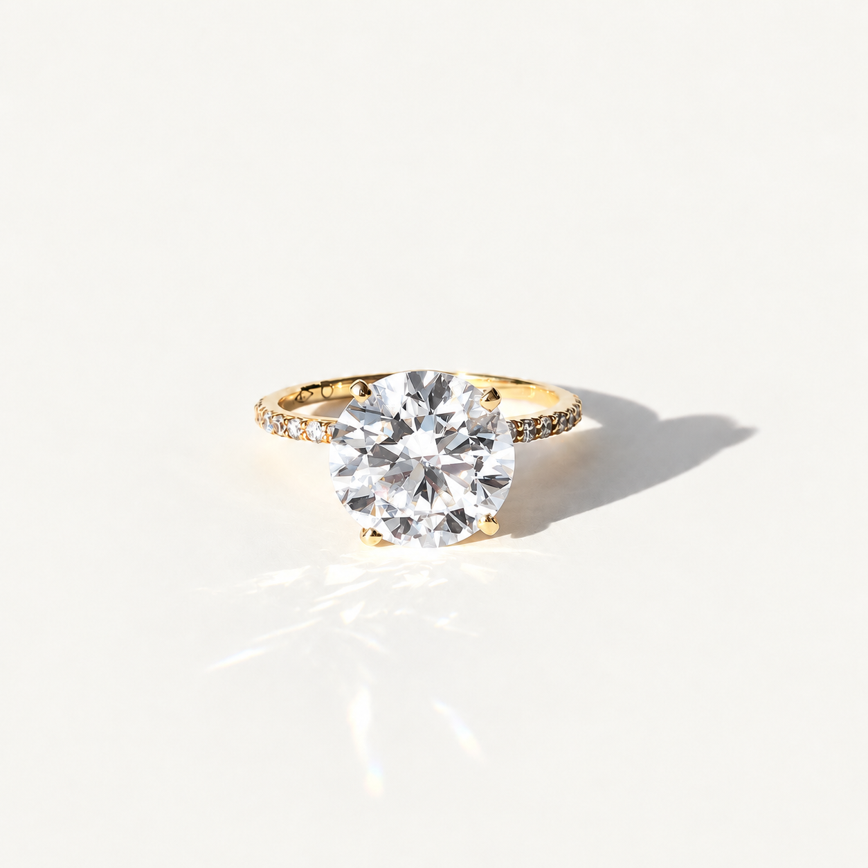 A yellow gold solitaire engagement ring with a large round brilliant-cut clear 4ct diamond center stone and a pavé-set diamond band, photographed on a clean white background with a soft shadow.