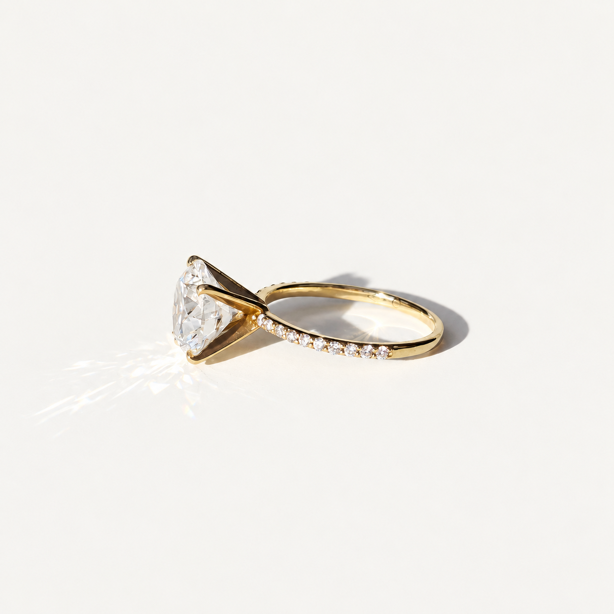 A yellow gold solitaire engagement ring with a large round brilliant-cut clear 4ct diamond center stone and a pavé-set diamond band, photographed on a clean white background with a soft shadow.