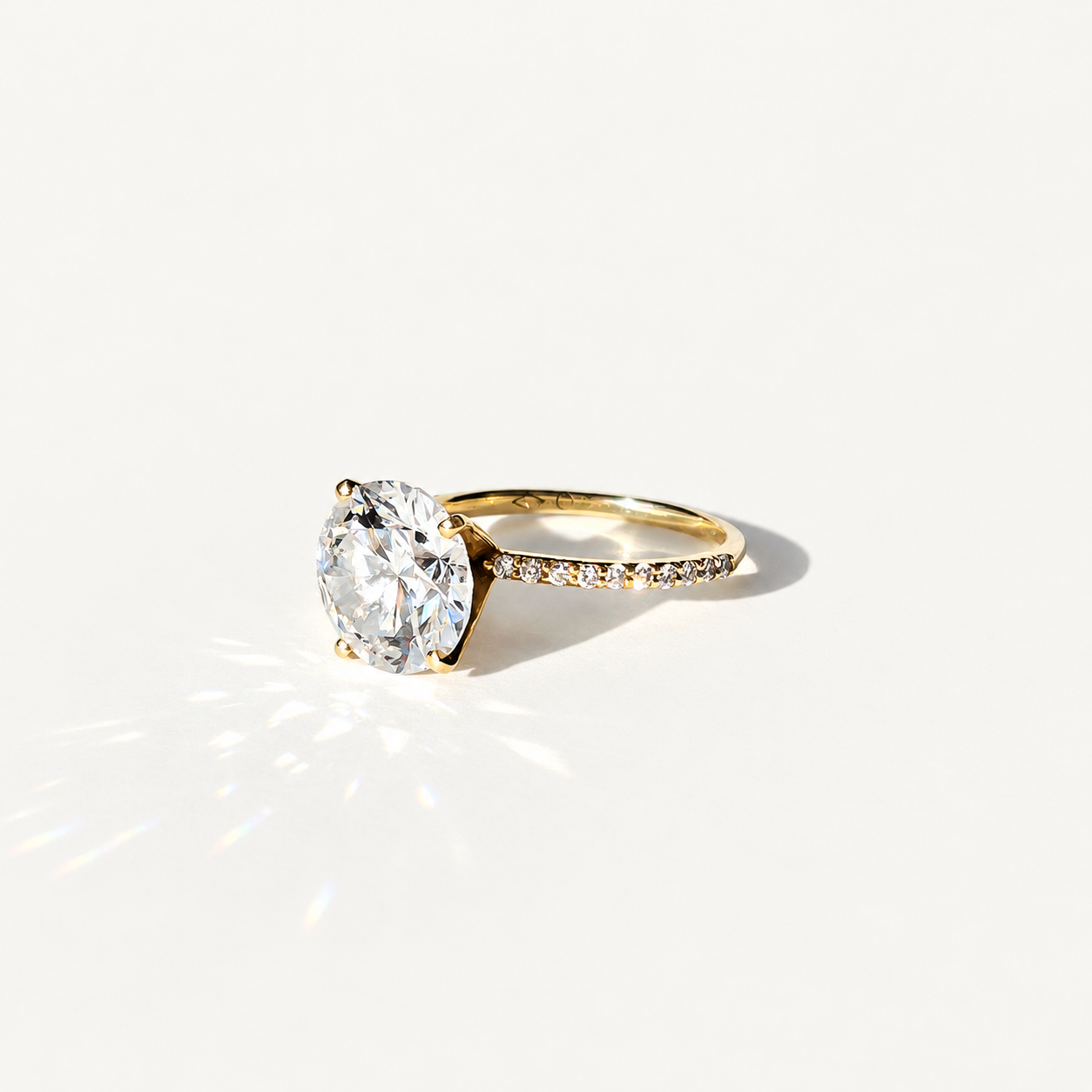 A yellow gold solitaire engagement ring with a large round brilliant-cut clear 4ct diamond center stone and a pavé-set diamond band, photographed on a clean white background with a soft shadow.