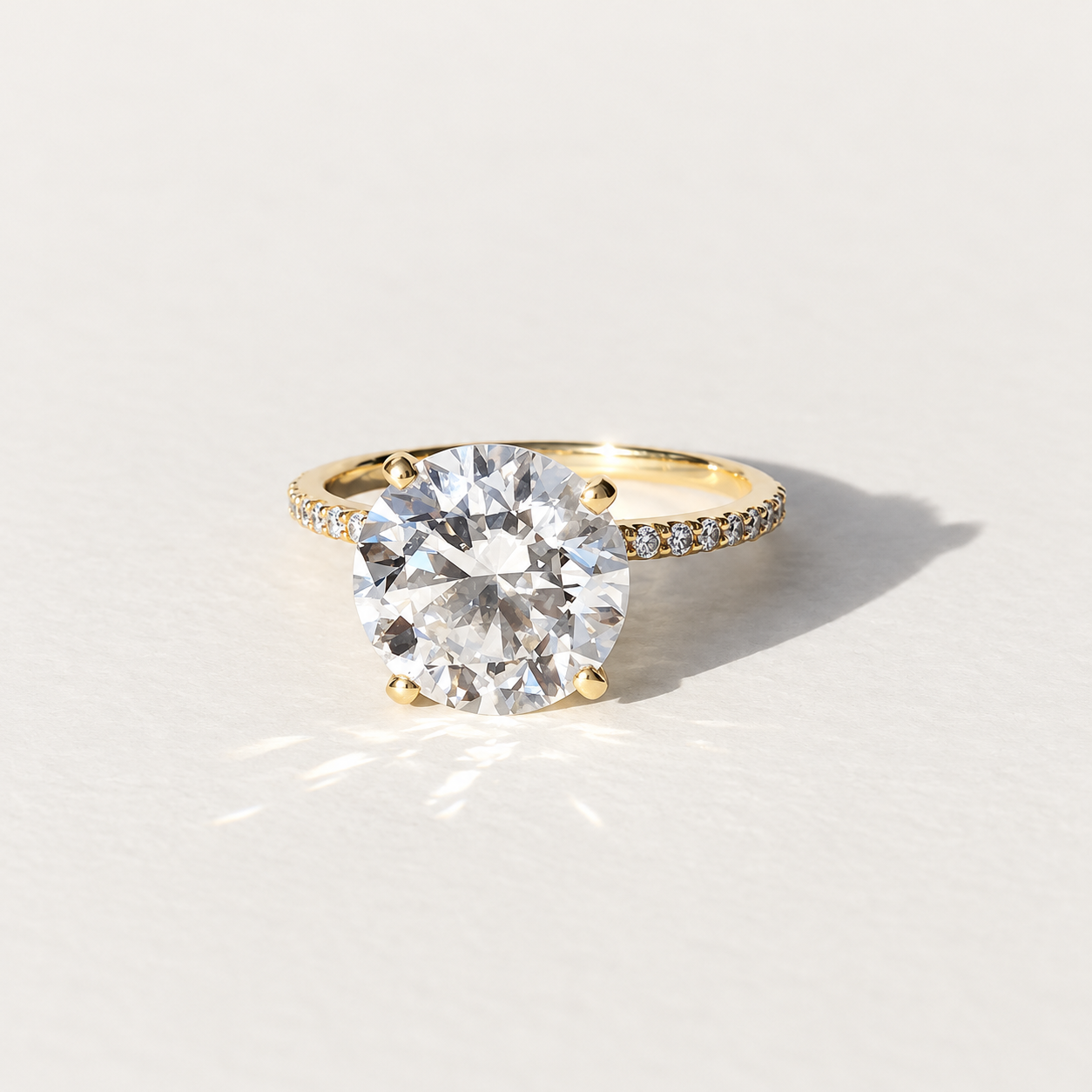 A yellow gold solitaire engagement ring with a large round brilliant-cut clear 4ct diamond center stone and a pavé-set diamond band, photographed on a clean white background with a soft shadow.
