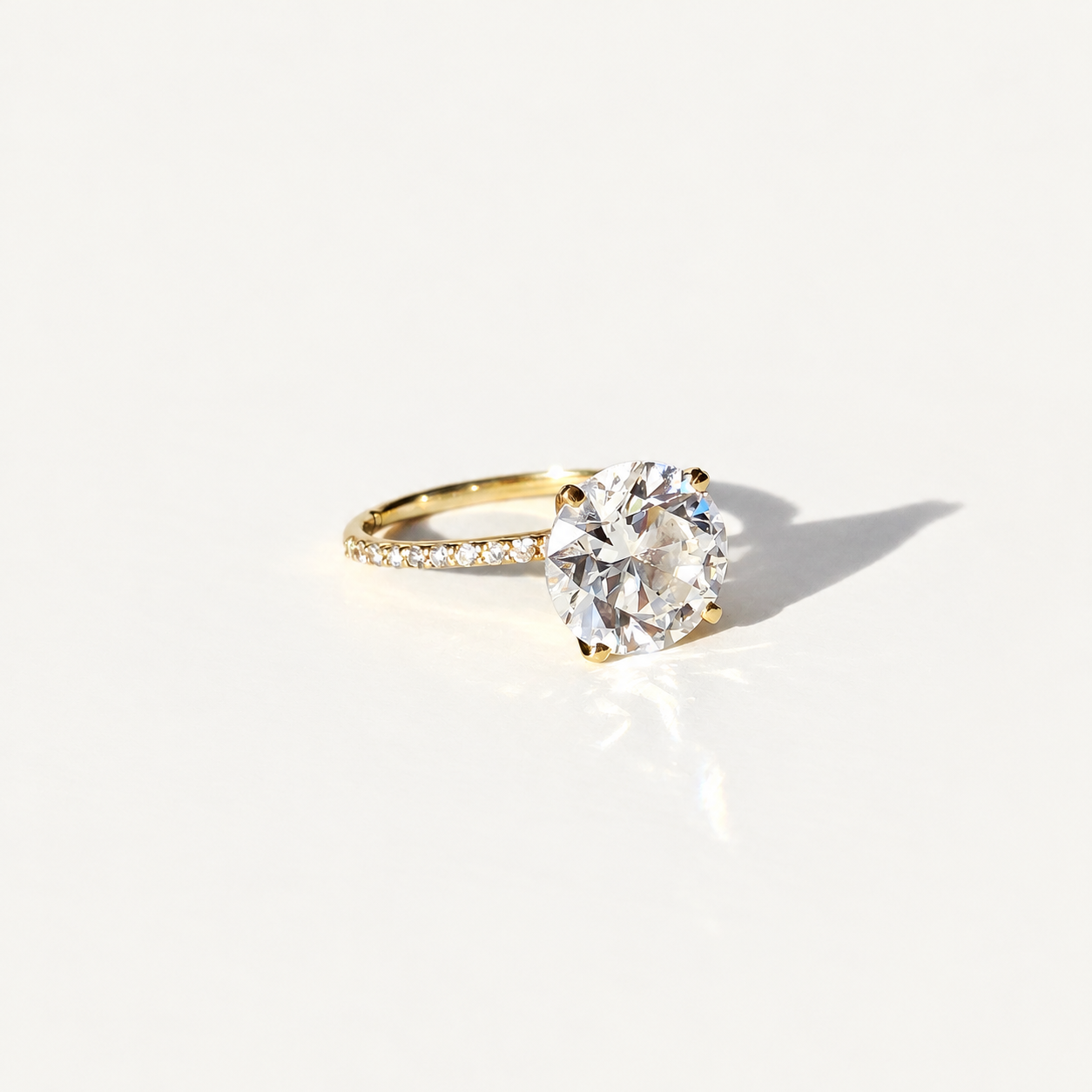 A yellow gold solitaire engagement ring with a large round brilliant-cut clear 4ct diamond center stone and a pavé-set diamond band, photographed on a clean white background with a soft shadow.